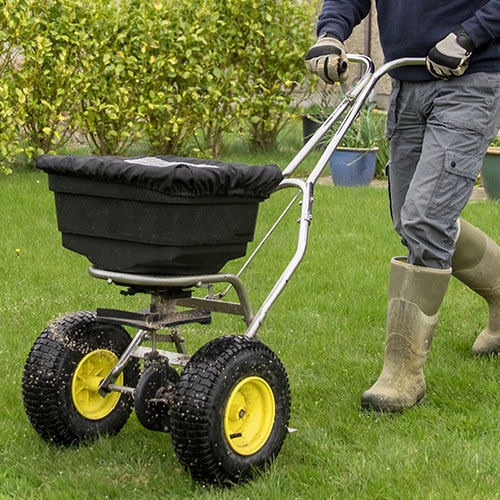 home Landscaper fertilizing lawn with a spreader and rain boots