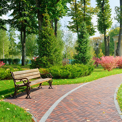 home City park with colorful flowers, bushes, a brick walkway and a bench